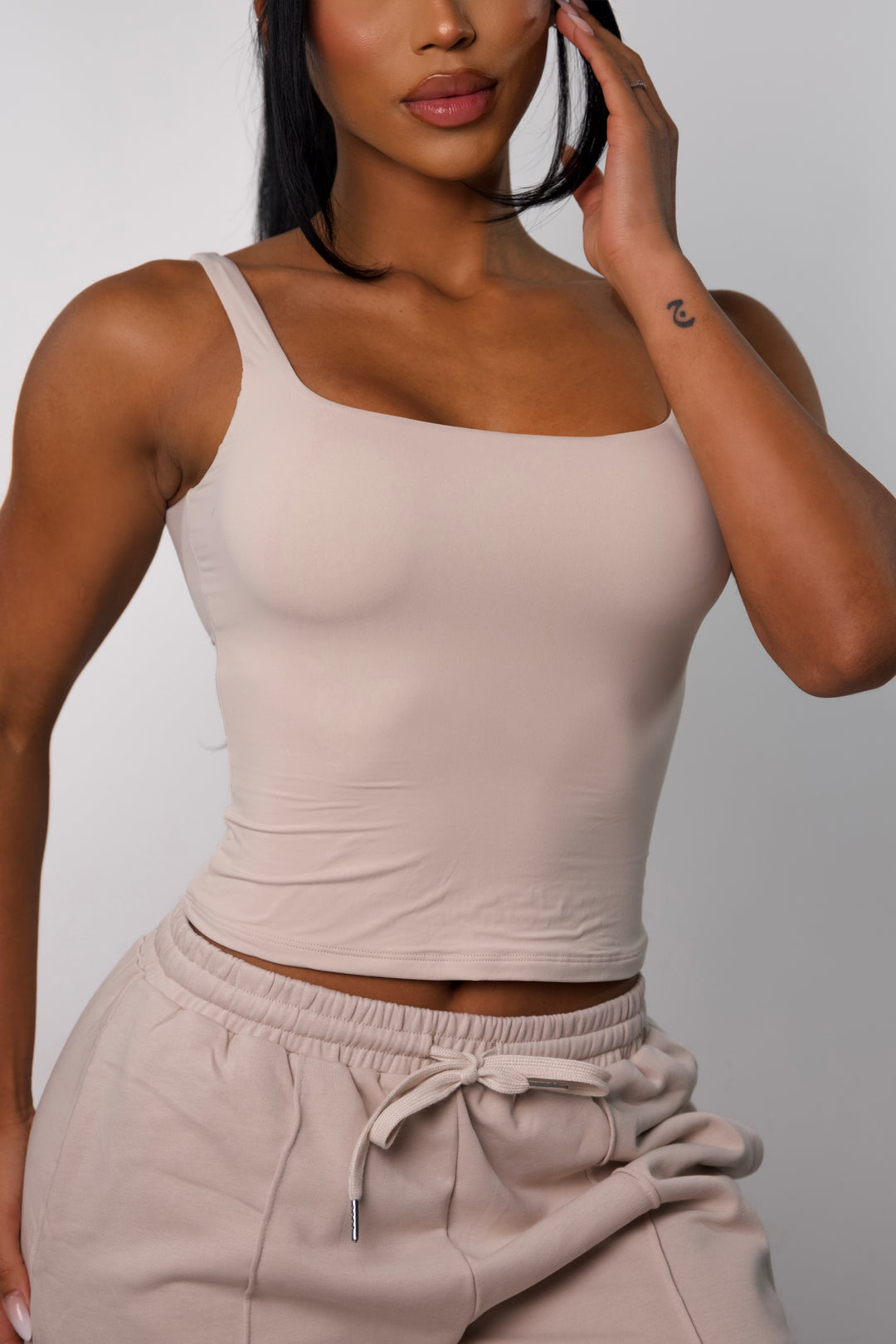 Front view of model wearing beige workout tank top for women with seamless, sculpting fit and breathable fabric.