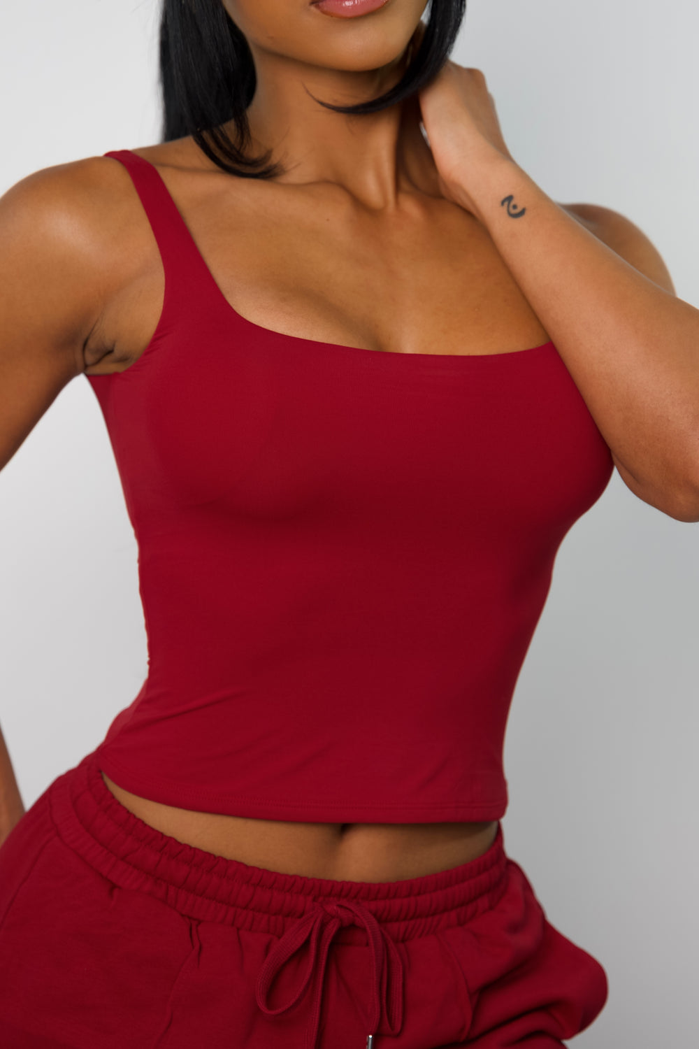Close-up front view of model wearing a red activewear tank top, hips high.