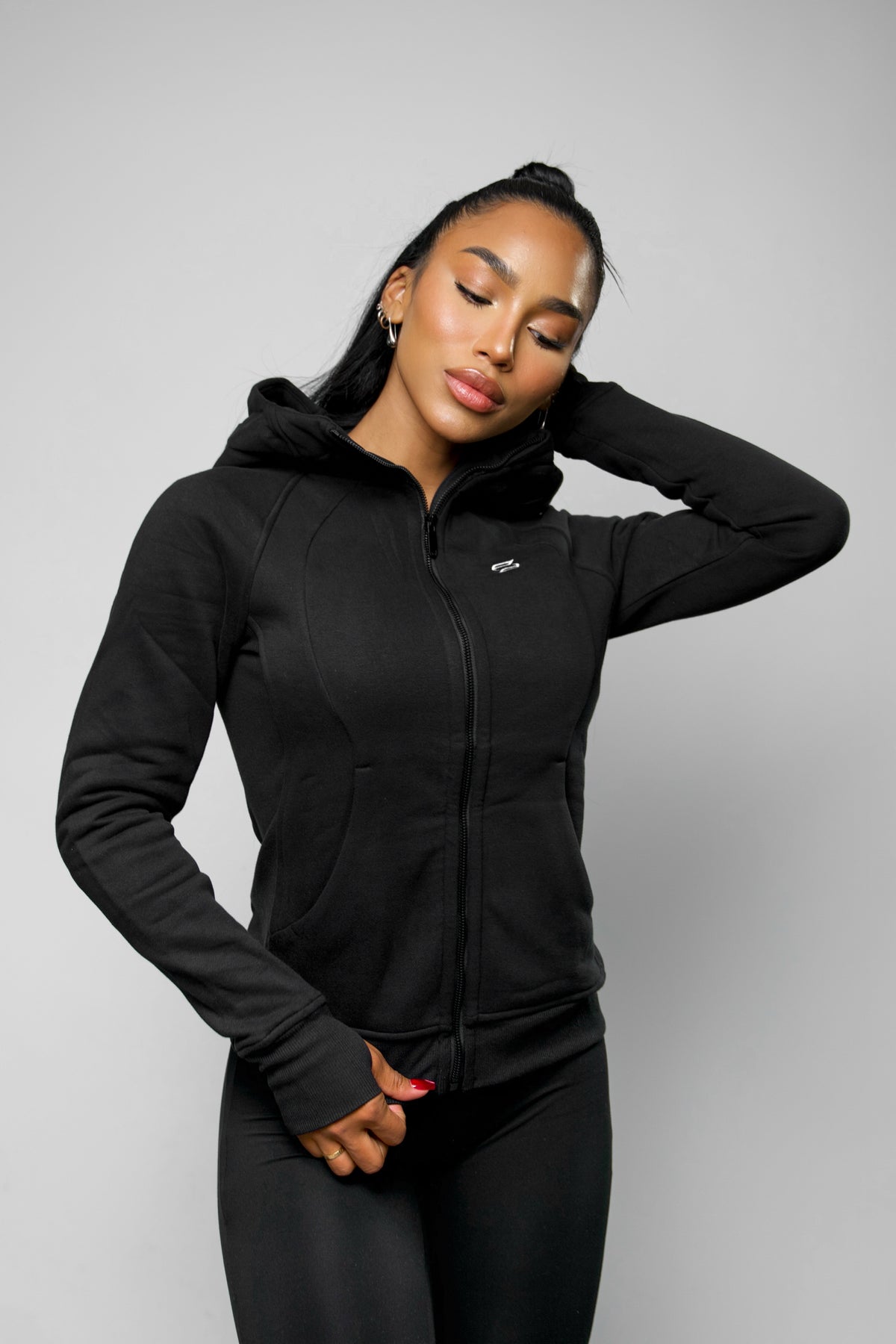 Front view of model wearing a black hooded jacket for women, fully zipped for a workout or loungewear look.